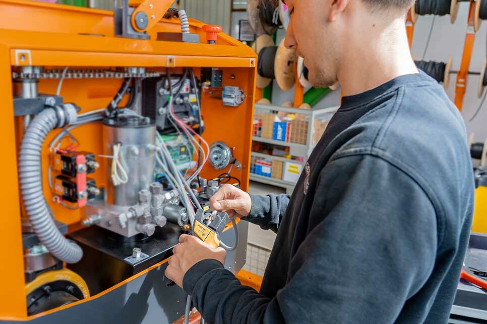 Mechatroniker Azubi isoliert Kabel mit einer Abisolierzange direkt an einem Flurförderfahrzeug während seiner Ausbildung bei Genkinger.
