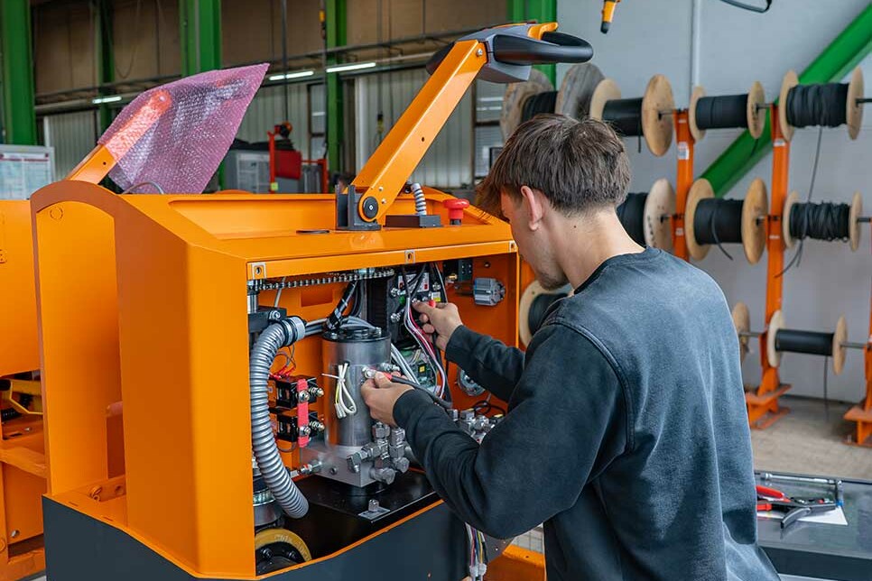 Mechatroniker Azubi verkabelt ein Flurförderfahrzeug in der Fertigung bei Genkinger und arbeitet dabei mit Unterstützung erfahrener Kollegen.