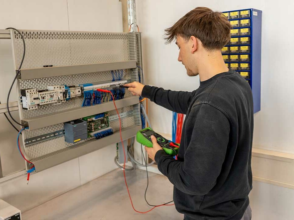 Auszubildender Elektroniker für Betriebstechnik misst Strom am Übungsschaltschrank während der Ausbildung bei Genkinger.