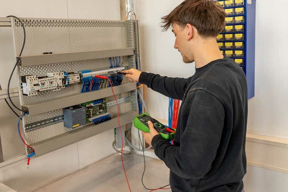 Auszubildender Elektroniker für Betriebstechnik misst Strom am Übungsschaltschrank während der Ausbildung bei Genkinger.