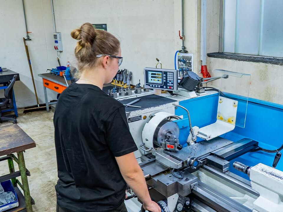 Auszubildende Industriemechanikerin arbeitet konzentriert an einer Drehbank und fertigt ein Werkstück im Rahmen ihrer Ausbildung bei Genkinger.