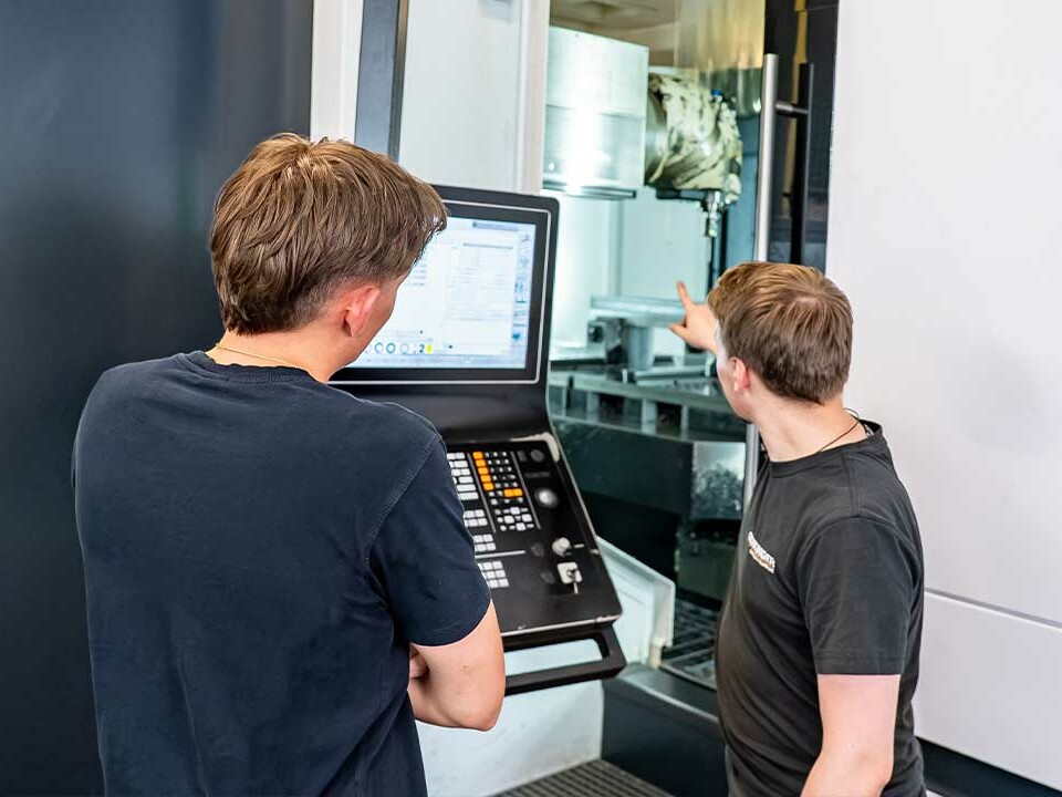 Ausbilder Janik erklärt einem Auszubildenden die Bedienung einer CNC-Maschine im Rahmen der Industriemechaniker-Ausbildung bei Genkinger.