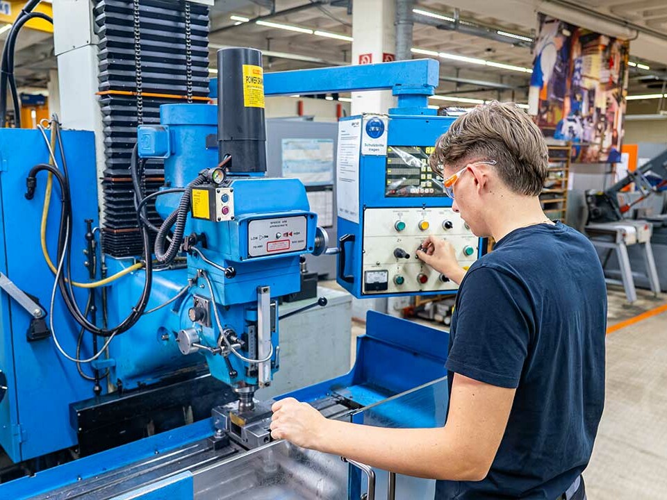 Auszubildende Industriemechanikerin bei Genkinger bearbeitet ein Metallbauteil an einer Fräsmaschine in der mechanischen Fertigung und trägt dabei eine Schutzbrille.