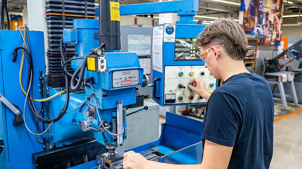 Auszubildende Industriemechanikerin bei Genkinger bearbeitet ein Metallbauteil an einer Fräsmaschine in der mechanischen Fertigung und trägt dabei eine Schutzbrille.