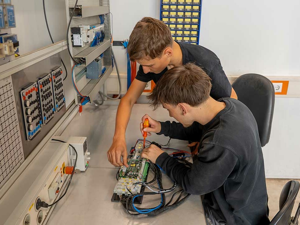 Zwei Auszubildender Elektroniker für Betriebstechnik arbeiten an einer Stromverteiler-Platine während ihrer Ausbildung bei Genkinger.