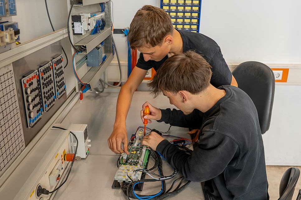 Zwei Auszubildender Elektroniker für Betriebstechnik arbeiten an einer Stromverteiler-Platine während ihrer Ausbildung bei Genkinger.