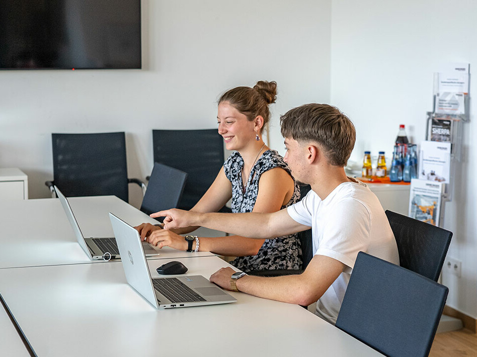 Die Auszubildenden Ramon und Laura von Genkinger sitzen gemeinsam in einem Meeting und besprechen Aufgaben im Rahmen ihrer Ausbildung als Industriekaufleute.