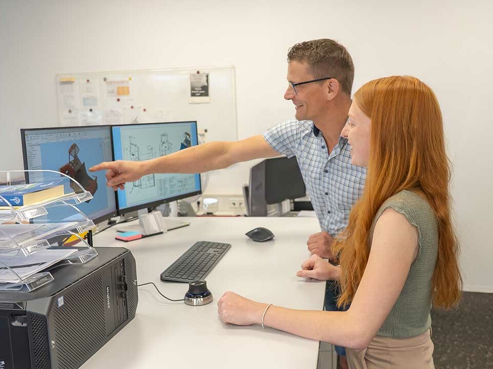 Ausbilder bespricht mit Auszubildender zur Technischen Produktdesignerin eine Konstruktion am Computer