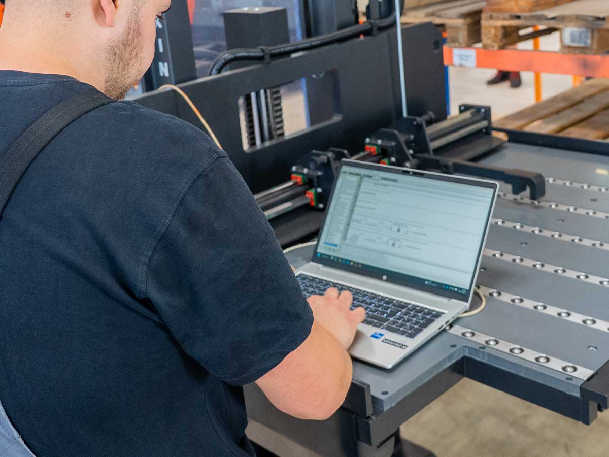 Servicetechniker von Genkinger verbindet einen Laptop mit einem Flurförderfahrzeug und führt eine digitale Diagnose sowie Servicearbeiten durch.
